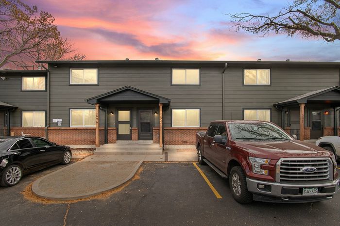Contemporary townhouse exterior with a sunset backdrop and parked vehicles in front.