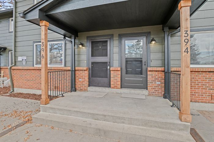 Inviting front porch with red brick and modern gray siding, featuring dual black doors and wood accents.