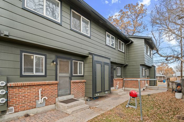 Charming two-story townhouse with green painted siding and red brick accents, featuring a small patio with a barbecue grill.