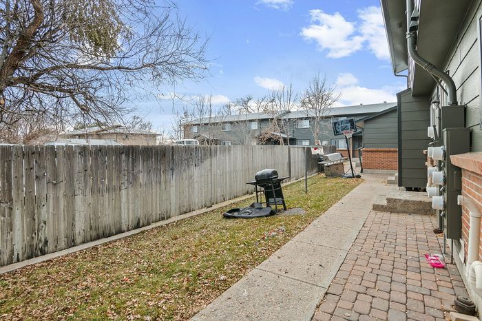 Peaceful backyard area featuring a grill, sidewalk, and basketball hoop against a blue sky.