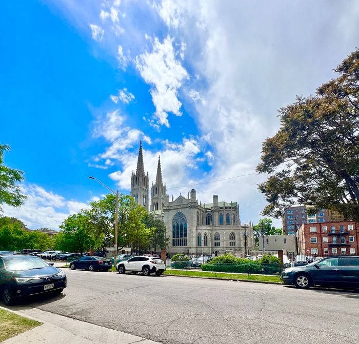 A picturesque street view featuring a grand historic building with towering spires and a clear blue sky.