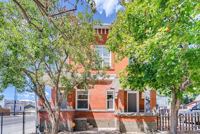 Charming brick house exterior with lush green trees and a bright blue sky.