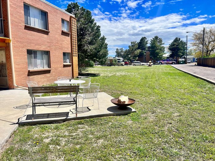 Charming apartment building with outdoor seating on a sunny day, featuring a lush green lawn.