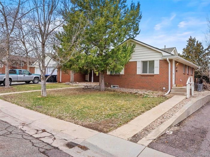 Charming brick home with manicured lawn and lush tree, nestled in a serene neighborhood.