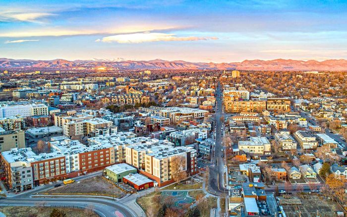 Breathtaking aerial view of a vibrant cityscape, showcasing a harmonious blend of urban architecture and scenic mountain backdrop at sunset.