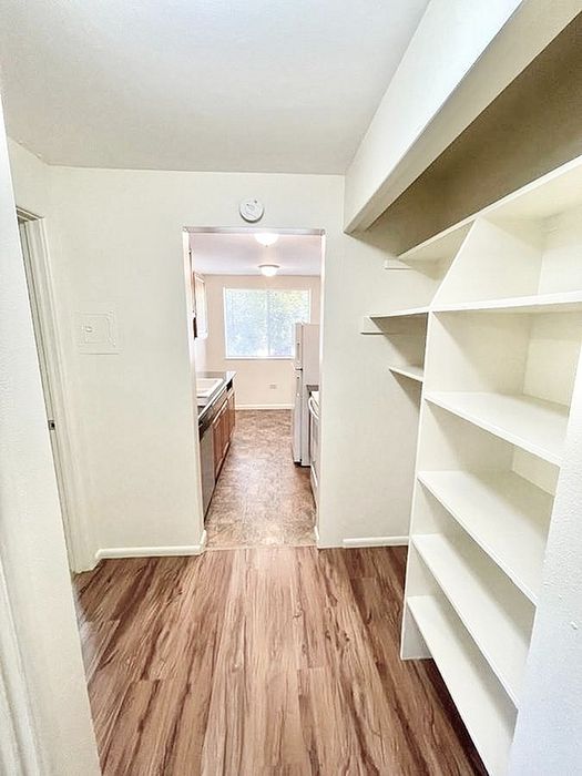 Inviting hallway with elegant wood flooring leading to a bright kitchen, featuring ample white shelving and natural light.