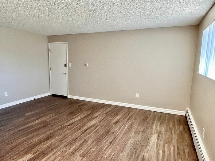 Inviting empty room with sleek hardwood floors, cream walls, and ample natural light from a large window, ideal for versatile decor opportunities.