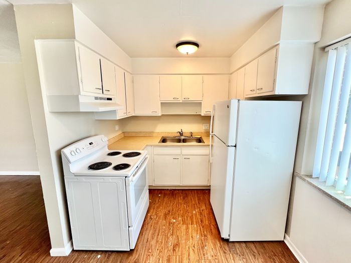 Charming kitchen with modern white cabinetry, efficient appliances, and warm wood-style flooring.