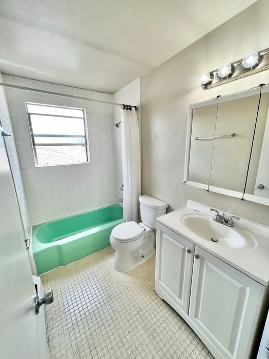 Bright and inviting bathroom with a retro green bathtub, elegant white tiles, and a modern vanity.