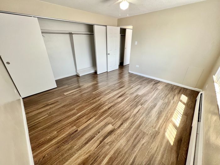 Bright and spacious bedroom with elegant wood flooring and abundant closet space, featuring a ceiling fan for comfort.