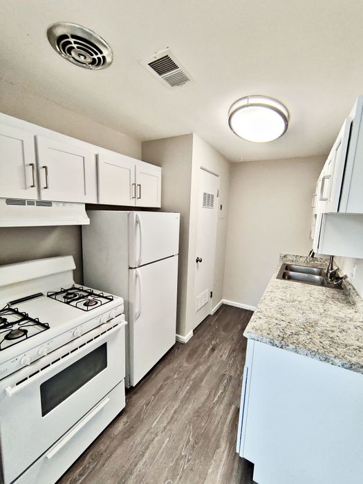 Modern kitchen with sleek granite countertops, white cabinetry, and a full-size refrigerator, offering a bright and inviting space.
