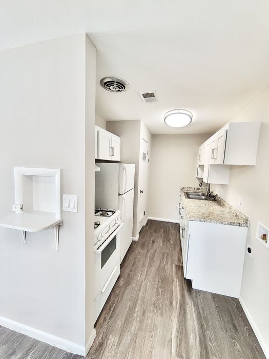 Bright and modern galley kitchen with sleek white cabinetry, granite countertops, and elegant wood flooring.