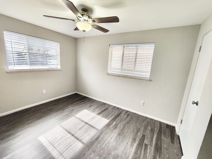 Bright and airy room with elegant dark wood flooring and modern ceiling fan, perfect for a cozy bedroom setup.