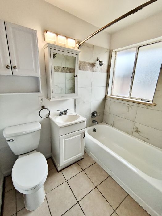 Modern bathroom featuring sleek white fixtures, a chic mirrored cabinet, and elegant tile flooring.