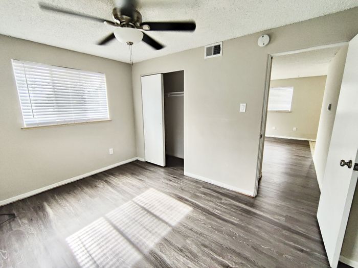 Bright and airy bedroom with sleek hardwood floors and natural light, featuring a ceiling fan and spacious closet.