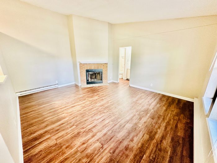 Bright and inviting living room with a cozy brick fireplace and elegant wooden flooring, perfect for relaxing evenings.