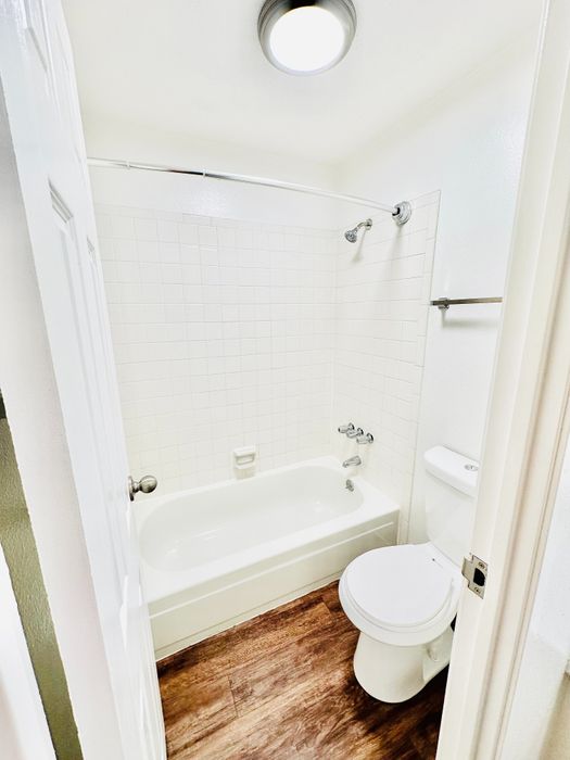 Bright and modern bathroom featuring a sleek bathtub, white tiled walls, and elegant wood flooring, creating a refreshing and stylish space.