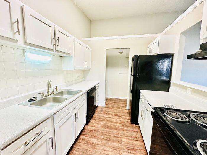 Modern galley kitchen with sleek white cabinetry, dual sinks, and elegant wood flooring.