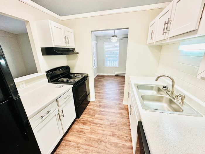 Inviting kitchen with modern appliances, elegant white cabinetry, and sleek countertops leading to a sunlit dining area with hardwood flooring.