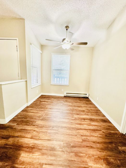 Bright room with elegant wooden flooring, featuring large windows and a modern ceiling fan.