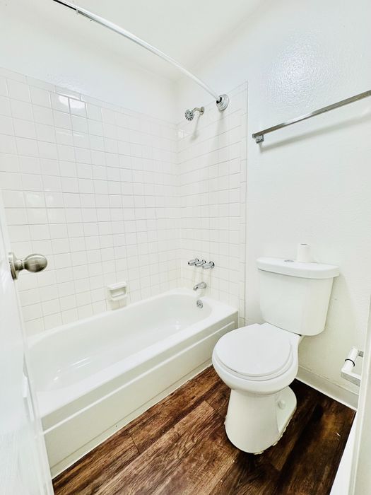 Bright and modern bathroom featuring a sleek bathtub, elegant white tiles, and rich wooden flooring for a luxurious touch.