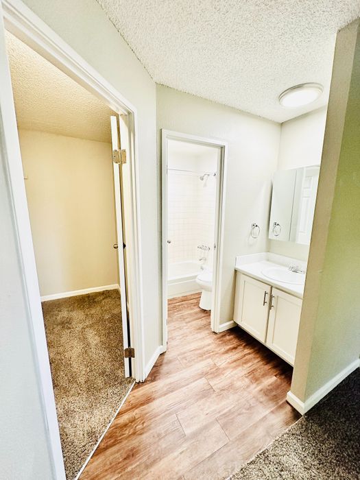 Bright hallway featuring elegant wood flooring and access to a cozy carpeted room and a pristine bathroom.