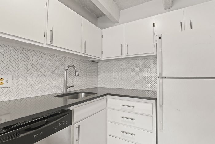 Modern kitchen with sleek white cabinets, elegant herringbone backsplash, and polished countertop, offering a stylish cooking space.