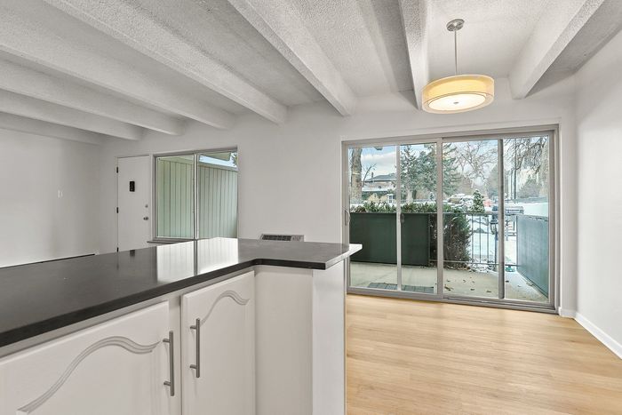 Modern apartment interior showcasing a sleek kitchen countertop leading to a bright dining area with large sliding glass doors opening to a cozy balcony view.