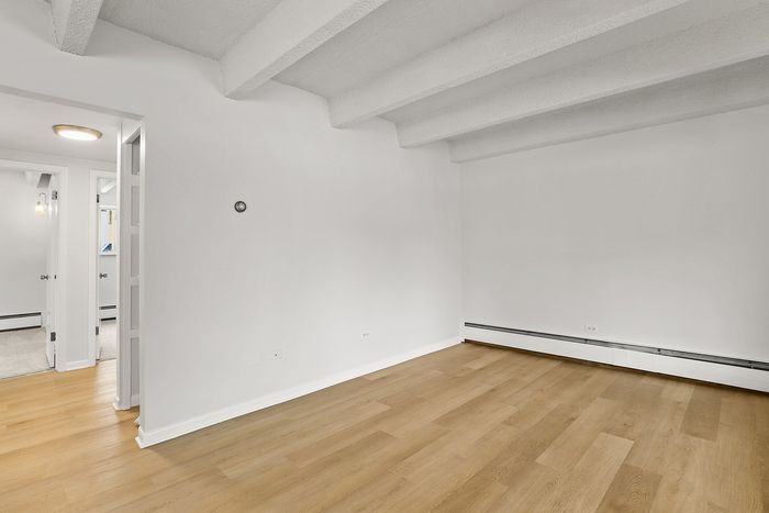 Bright and airy room with beautiful wood flooring, featuring modern minimalist design and exposed ceiling beams.