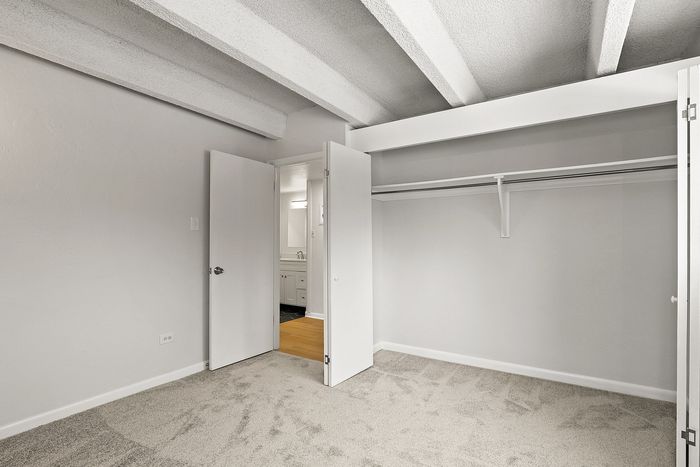 Bright bedroom with ample closet space, accented by elegant grey carpeting and exposed beam ceilings.