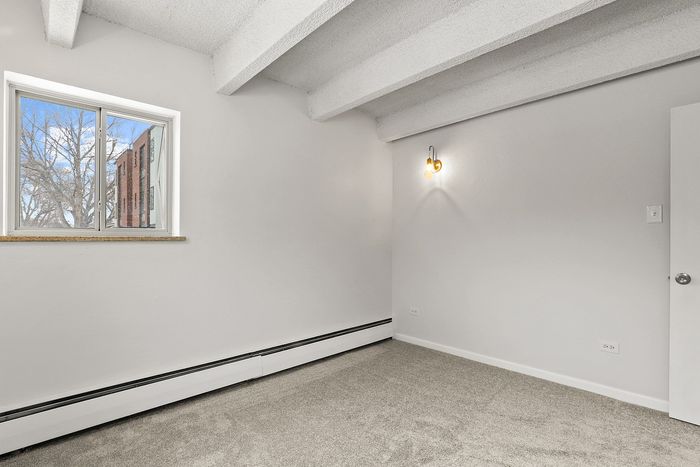 Bright and cozy room with large window, plush carpet, and modern sconce light, perfect for creating a personal retreat.