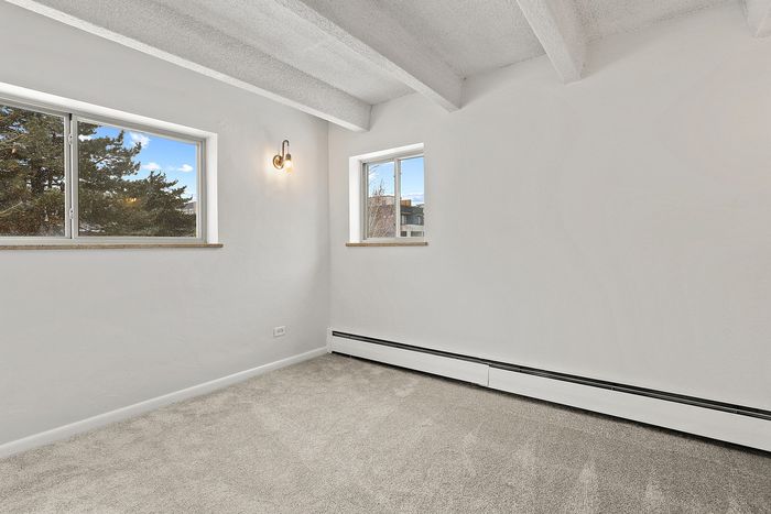Bright, minimalist room with plush carpet, two large windows, and stylish wall light, offering a cozy and inviting atmosphere.