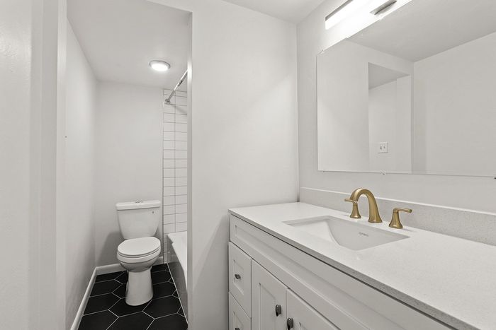 Elegant and modern bathroom featuring a pristine white vanity with stylish gold fixtures, a large mirror, and a sleek shower area.