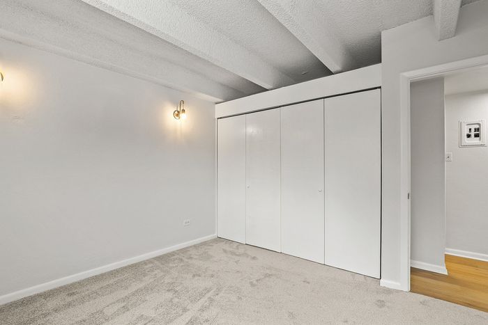 Bright room with soft carpet, modern overhead beams, and sleek built-in closet for stylish living.