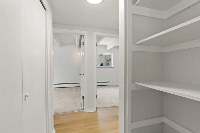 Bright and inviting hallway with open shelving and view into a cozy living space featuring natural wood flooring.
