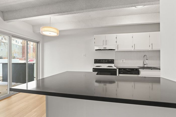 Elegant modern kitchen with sleek black countertops, white cabinetry, and a stylish backsplash, featuring large windows opening to a bright view.