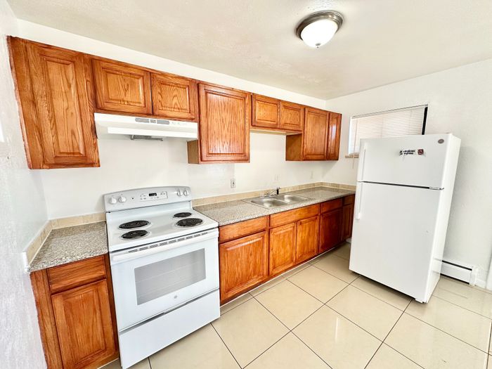 Modern kitchen with sleek granite countertops, wooden cabinets, and appliances including stove and refrigerator.