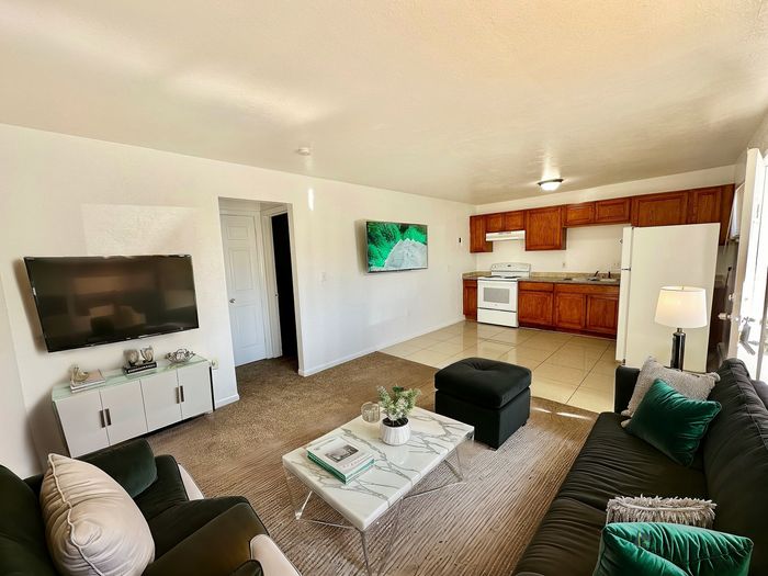 Inviting living space with plush seating, modern d&eacute;cor, and an elegant open kitchen featuring rich wood cabinets and bright lighting.