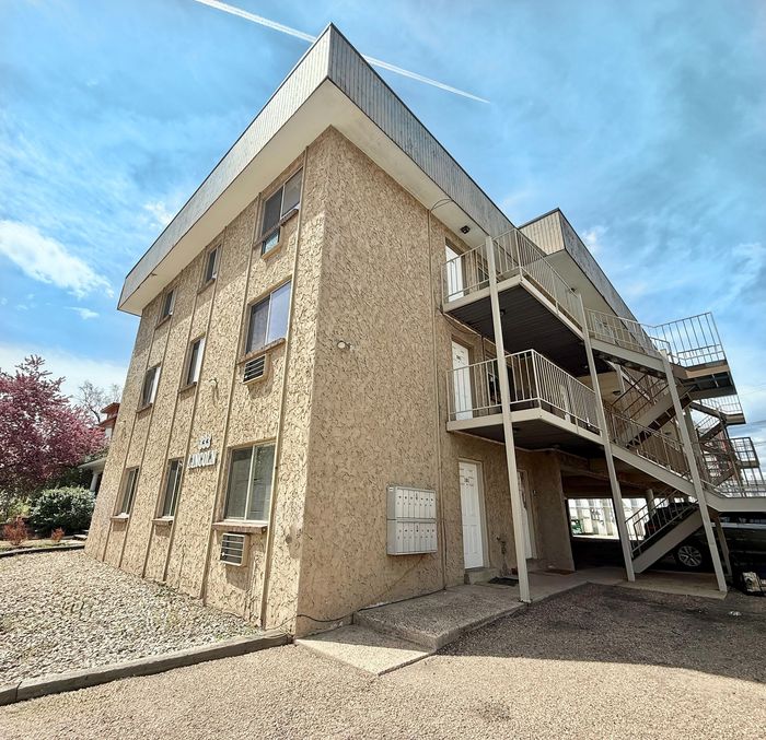 Charming three-story apartment building with modern staircases and textured exterior under a clear blue sky.