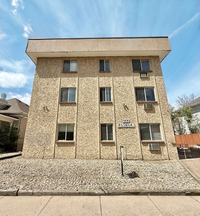 Charming three-story apartment building with textured exterior, surrounded by a neat stone landscape under a clear sky.