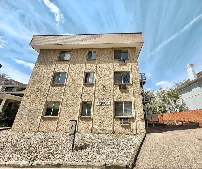 Charming three-story apartment building with unique textured facade and ample windows, located in a serene neighborhood, offering comfortable living spaces.