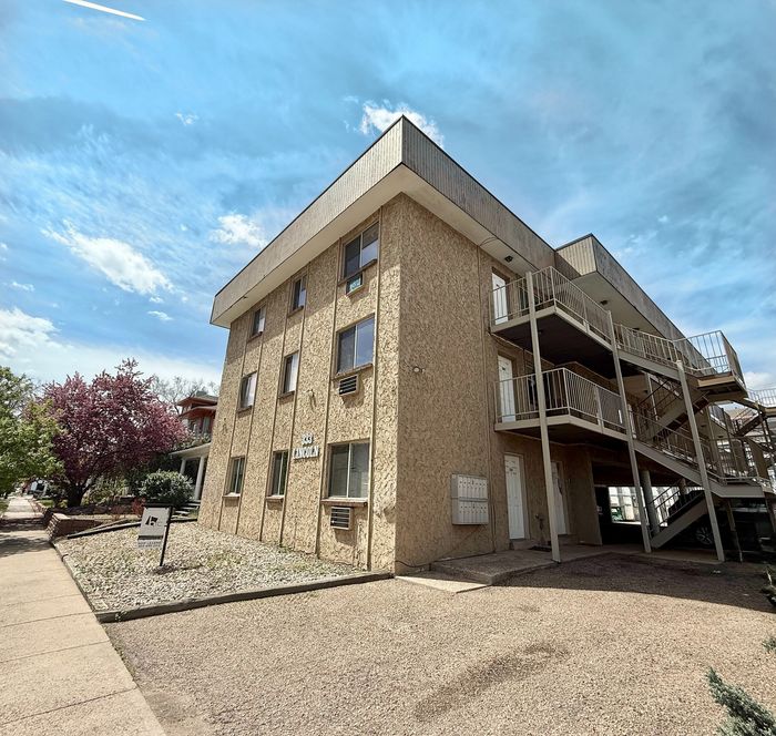 Charming apartment building with textured exterior, featuring outdoor staircases and scenic landscaping under a bright sky.