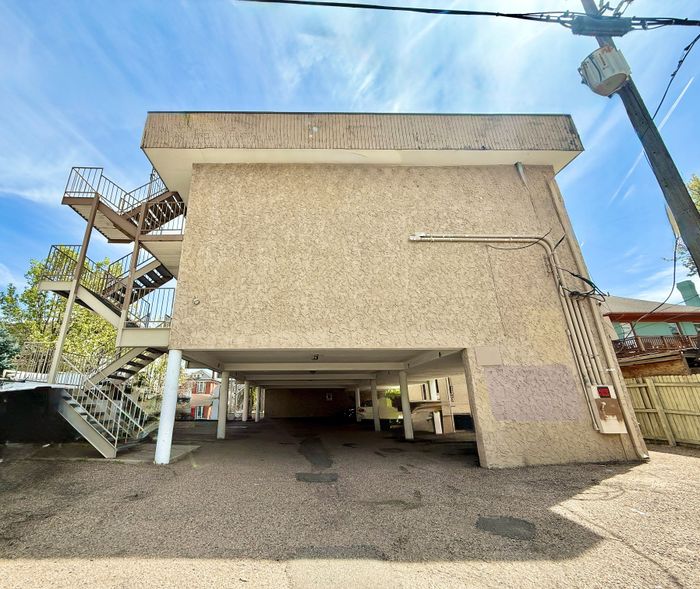 Charming urban apartment complex with stylish external staircase and ample parking under a bright blue sky.