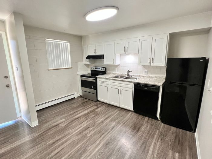Modern kitchen with sleek white cabinetry, granite countertops, and stainless steel appliances, accented by elegant dark flooring.