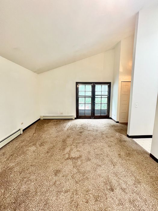 Bright and spacious living room with plush carpet and French doors leading to a serene outdoor view.