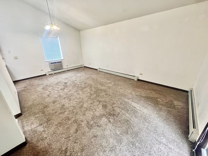 Bright, spacious room with plush carpeting, high ceiling, and a large window inviting natural light.