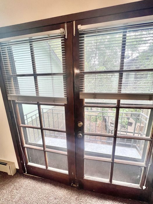 Charming glass French doors with elegant blinds opening to a private balcony surrounded by lush greenery.