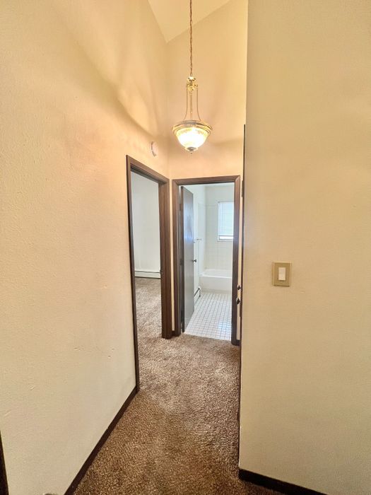 Inviting hallway with warm lighting leading to a cozy carpeted room and a pristine tiled bathroom.