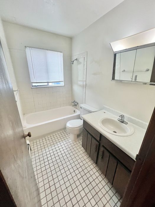 Bright bathroom featuring elegant white tiles, a classic bathtub, and a sleek vanity with ample storage.