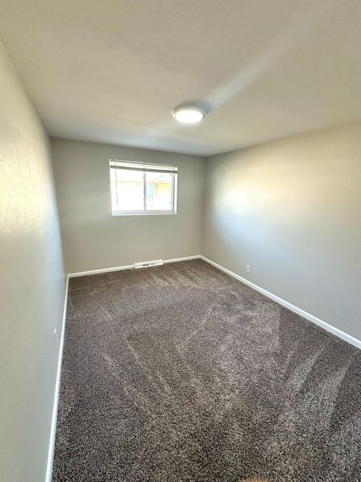 Cozy bedroom with plush carpeting, minimalist design, and a bright window for natural light.